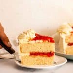 Placing a slice of vanilla cake with strawberry filling onto a white plate.