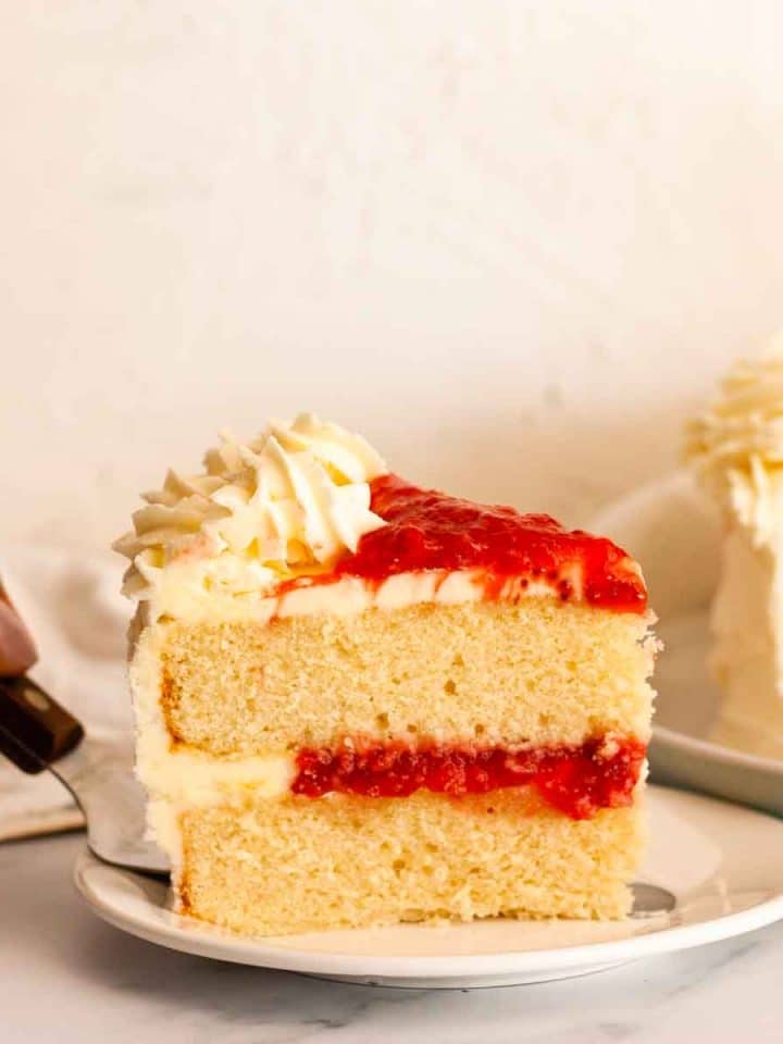 Placing a slice of vanilla cake with strawberry filling onto a white plate.
