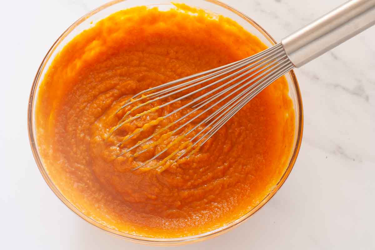 Whisking together pumpkin puree and eggs in a glass bowl.
