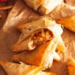 A close up of a bitten apple turnover with phyllo dough on top of other turnovers on brown parchment paper.