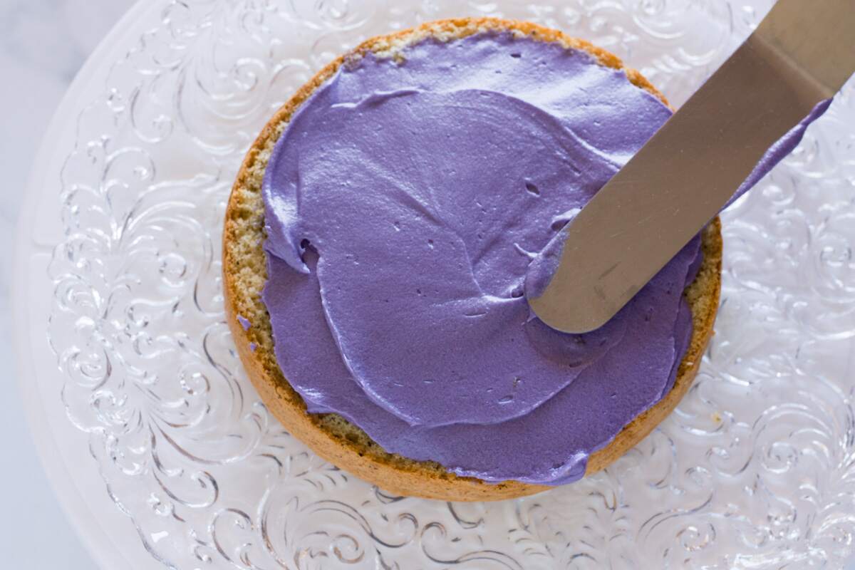 Adding lavender-colored frosting on a sponge cake layer with an offset spatula.