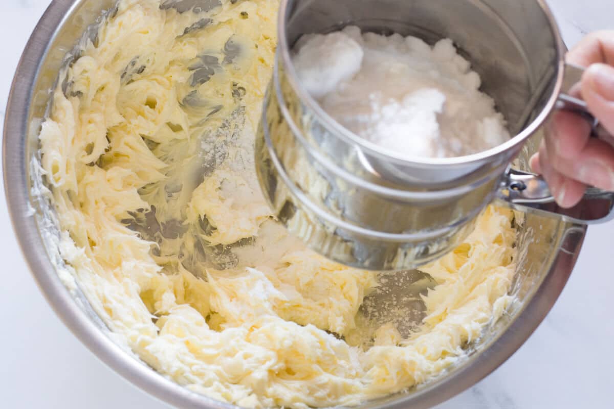 Sifting powdered sugar into creamed butter.