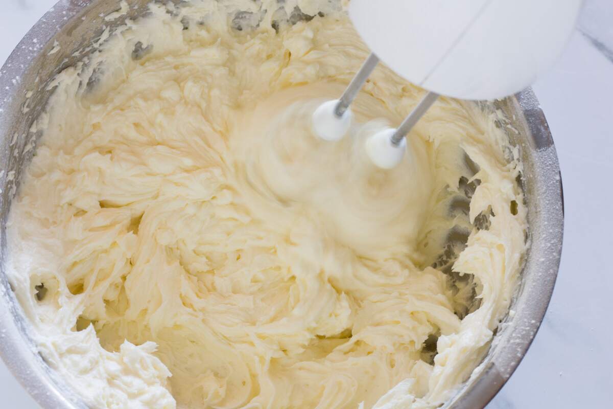 Beating vanilla and cream cheese into butter and powdered sugar mixture.
