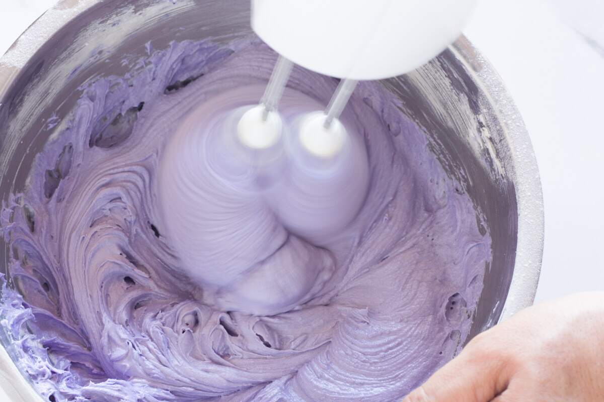 Beating cream cheese frosting to incorporate lavender food coloring.