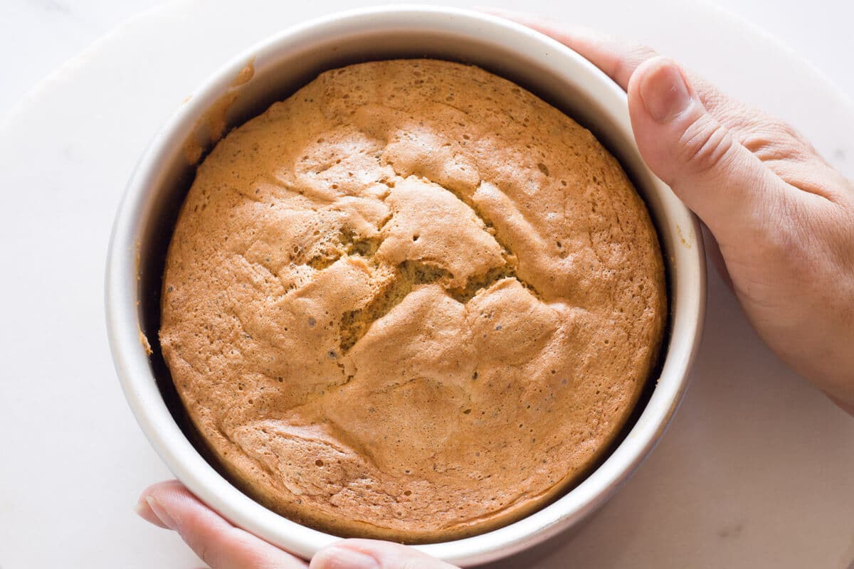 Two hands holding a baked sponge cake in a pan.