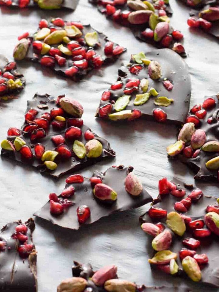 Chocolate pomegranate bark pieces on white parchment paper.