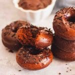 Two stacks of chocolate cake donuts with chocolate ganache and chocolate sprinkles on a gray surface.