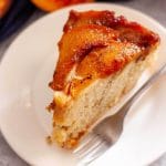 A closeup of a slice of caramel peach upside down cake on a white plate with a fork.