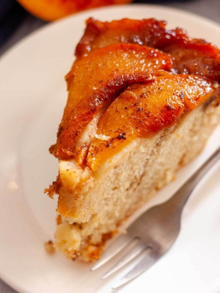 A closeup of a slice of caramel peach upside down cake on a white plate with a fork.