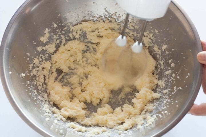 Beating butter and sugar together with a hand mixer in a metal bowl.