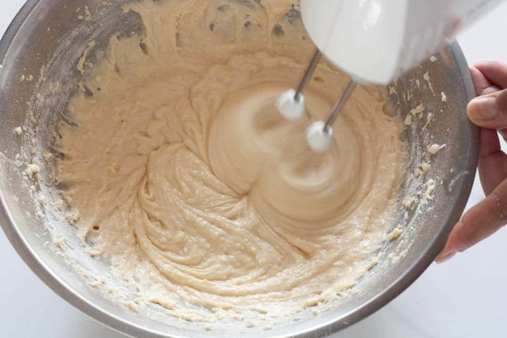 Beating dry and wet ingredients together with a hand mixer in a metal bowl.