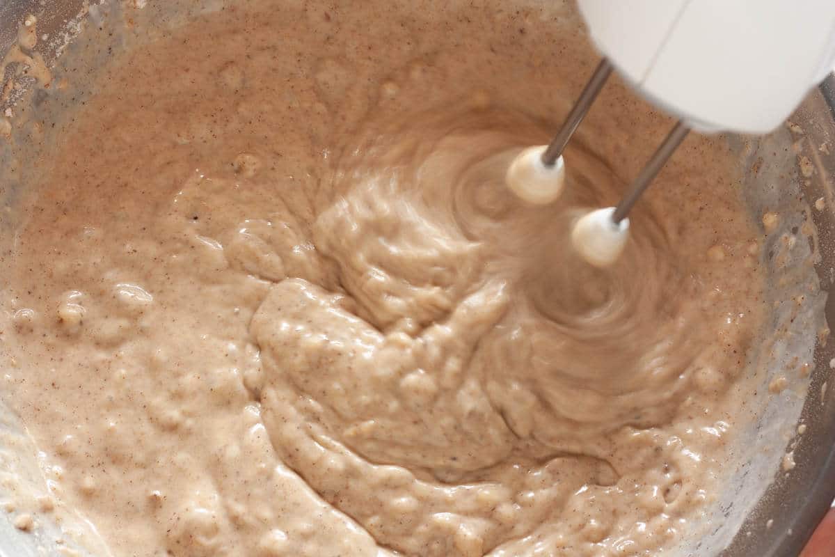 Beating dry ingredients with a mixer in a large mixing bowl.