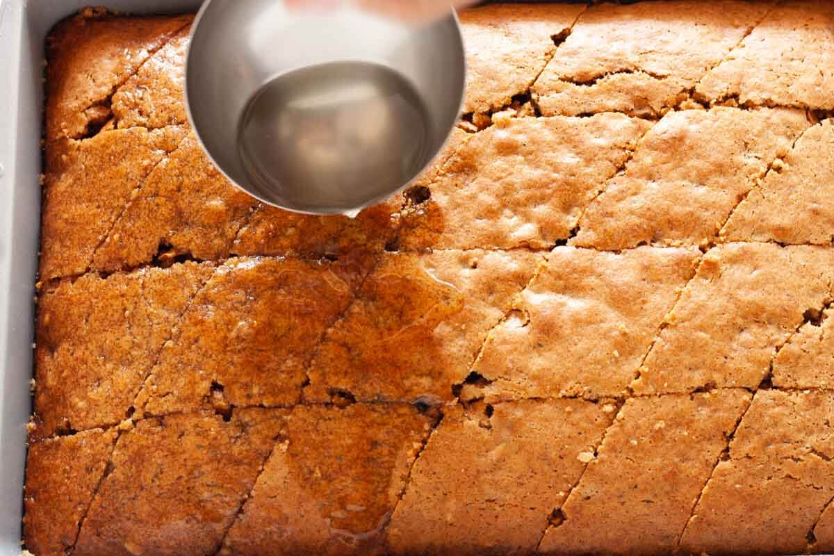Pouring syrup over baked karidopita cake with a ladle.