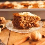 A close up of a slice of karidopita, Greek walnut cake, on a wooden surface next to walnuts and cinnamon sticks