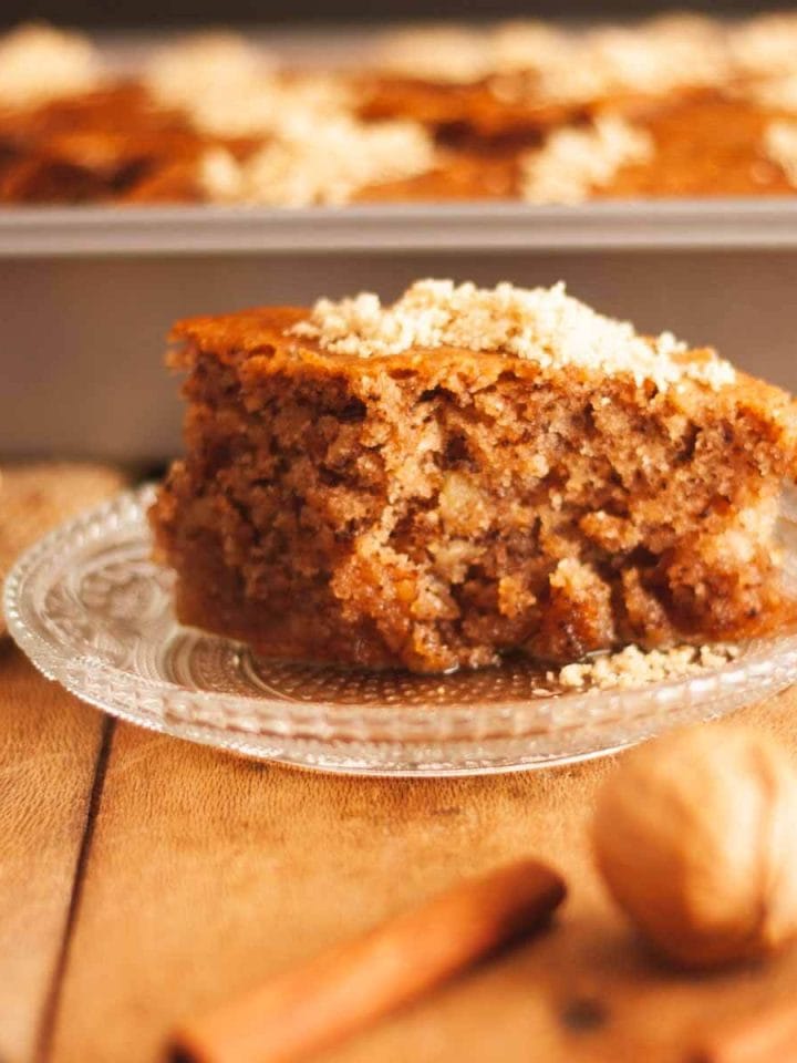 A close up of a slice of karidopita, Greek walnut cake, on a wooden surface next to walnuts and cinnamon sticks