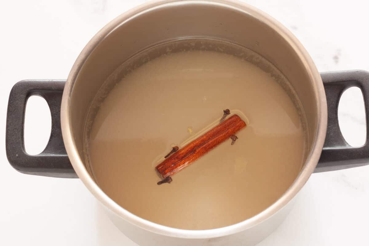 Sugar, water, cloves, and a cinnamon stick in a saucepan.