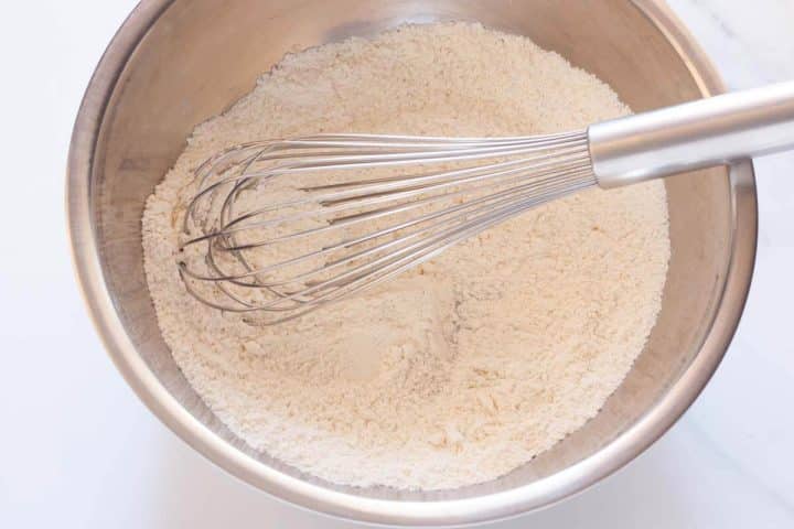 A large metal bowl with flour, baking powder and a whisk.