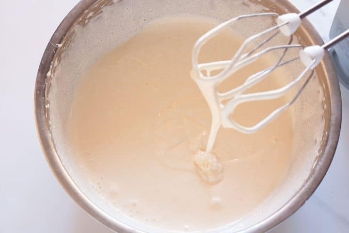 Beating eggs and sugar with a hand mixture to ribbon stage where the mixture is thick and is falling off beaters in ribbons.