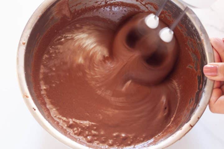 Beating the egg mixture with the cocoa mixture in a metal bowl with a hand mixer.