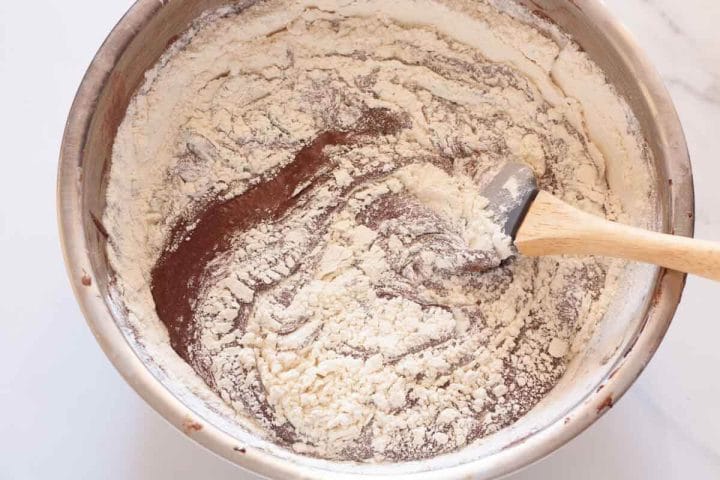 Gently folding flour mixture into chocolate mixture in a metal bowl with a silicone spatula.