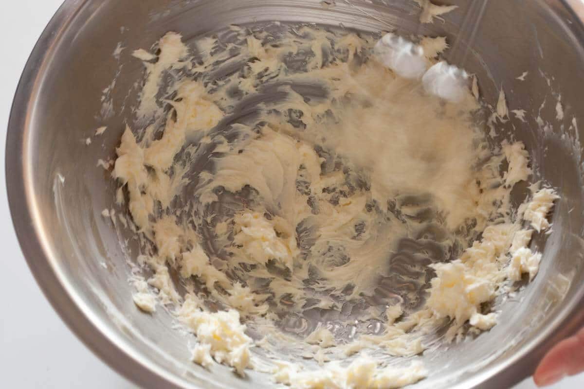 Beating butter in a metal bowl with a hand mixer.