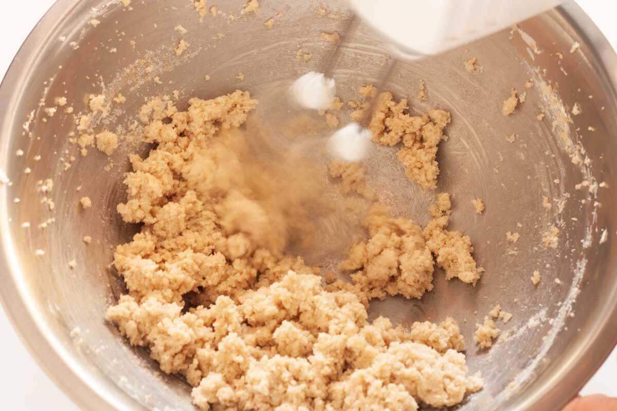 Beating sugar with butter in a metal bowl with a hand mixer.