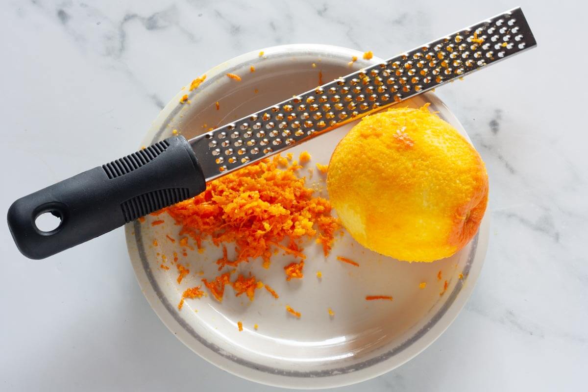 A zested orange on a plate with a microplane grater.