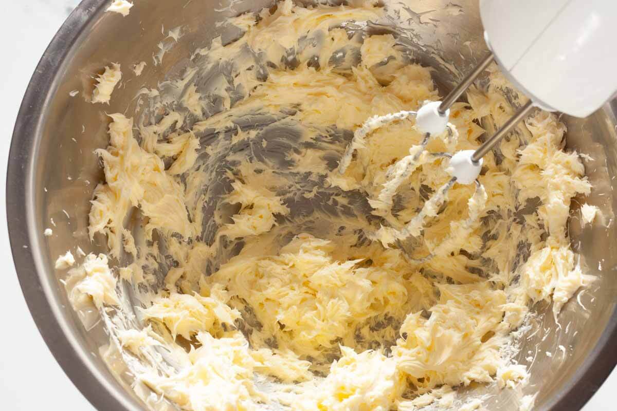 A hand mixer beating butter in a metal mixing bowl.