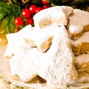 Kourabiedes on a white plate next to Christmas ornaments.