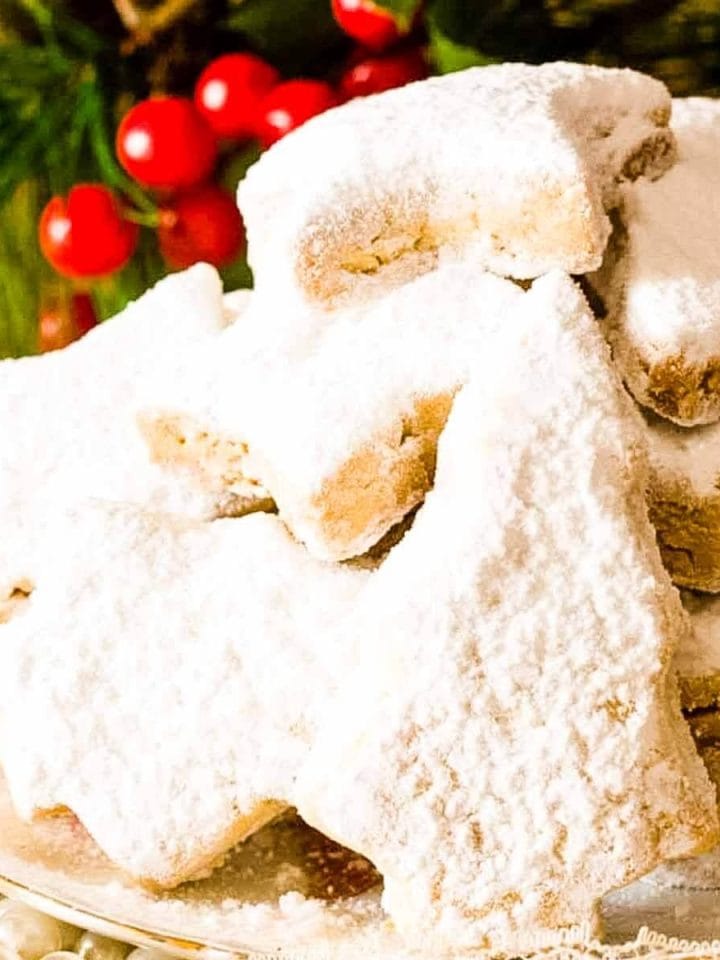 Kourabiedes on a white plate next to Christmas ornaments.