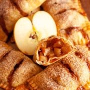 A close up of apple hand pies with puff pastry with a cut hand pie next to a sliced apple.