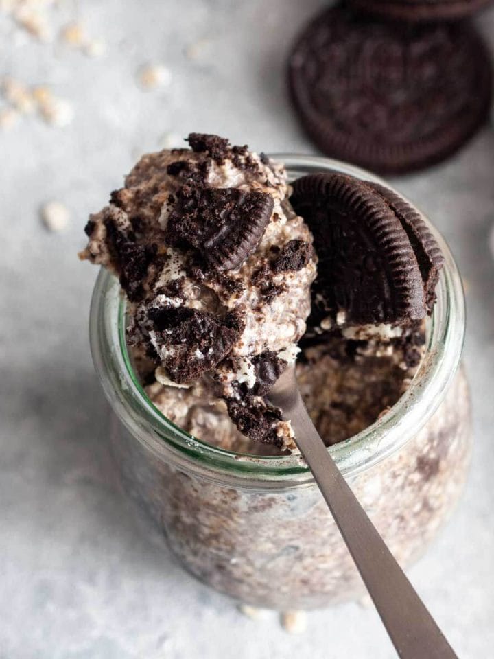 An overhead shot of Oreo overnight oats with crushed Oreo cookies on a spoon next to Oreo cookies and oats.