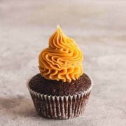 Peanut butter ganache swirled on a chocolate cupcake on a gray and white surface.