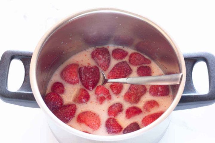 Strawberries, sugar, and lemon juice in a pan with cornstarch and water with a spoon.