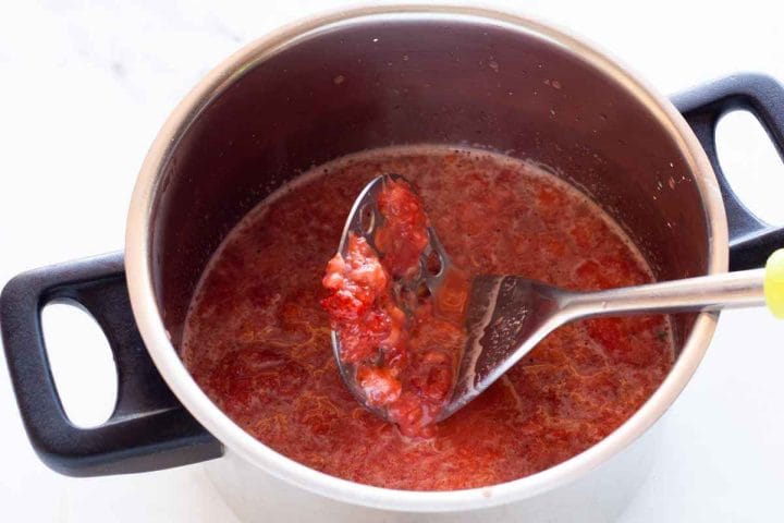 Mashing strawberries in a saucepan with a potato masher.