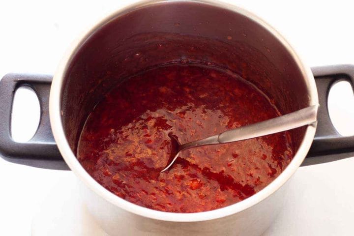 Cooked strawberry filling in a saucepan with a spoon.