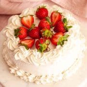 A strawberry whipped cream cake on a marble surface next to a pink towel and topped with fresh strawberries.