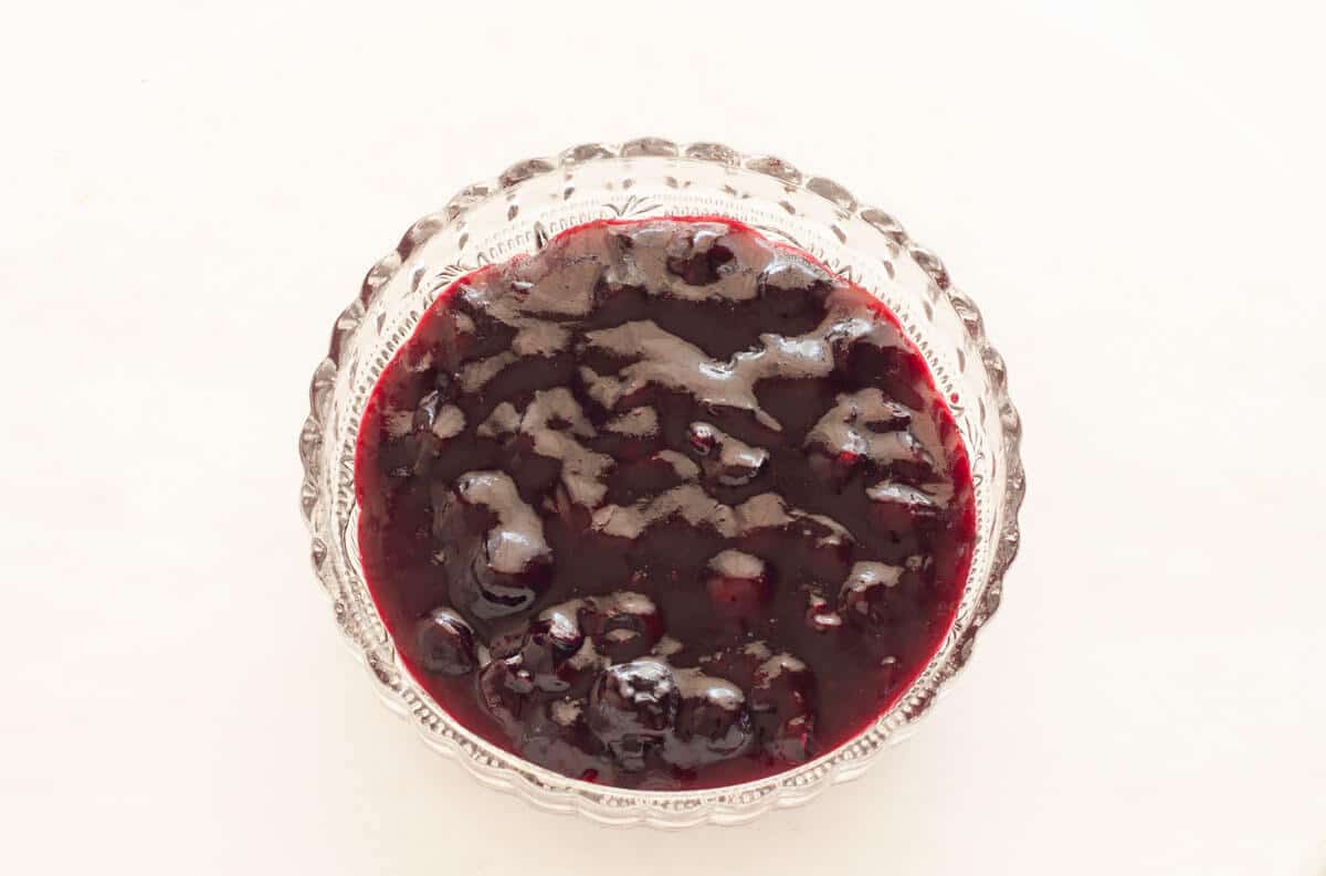 Blueberry cake filling in a glass bowl on a white surface.