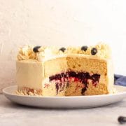 A close-up of a two-layer vanilla cake with blueberry filling on a white plate.