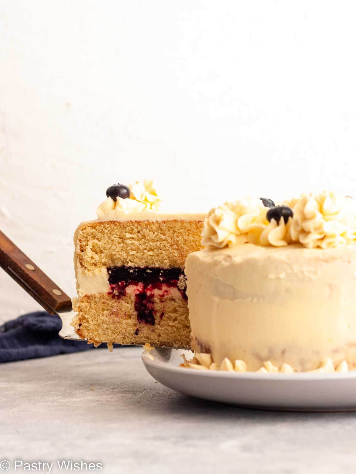 A slice of vanilla cake with blueberry filling on a cake slicer.
