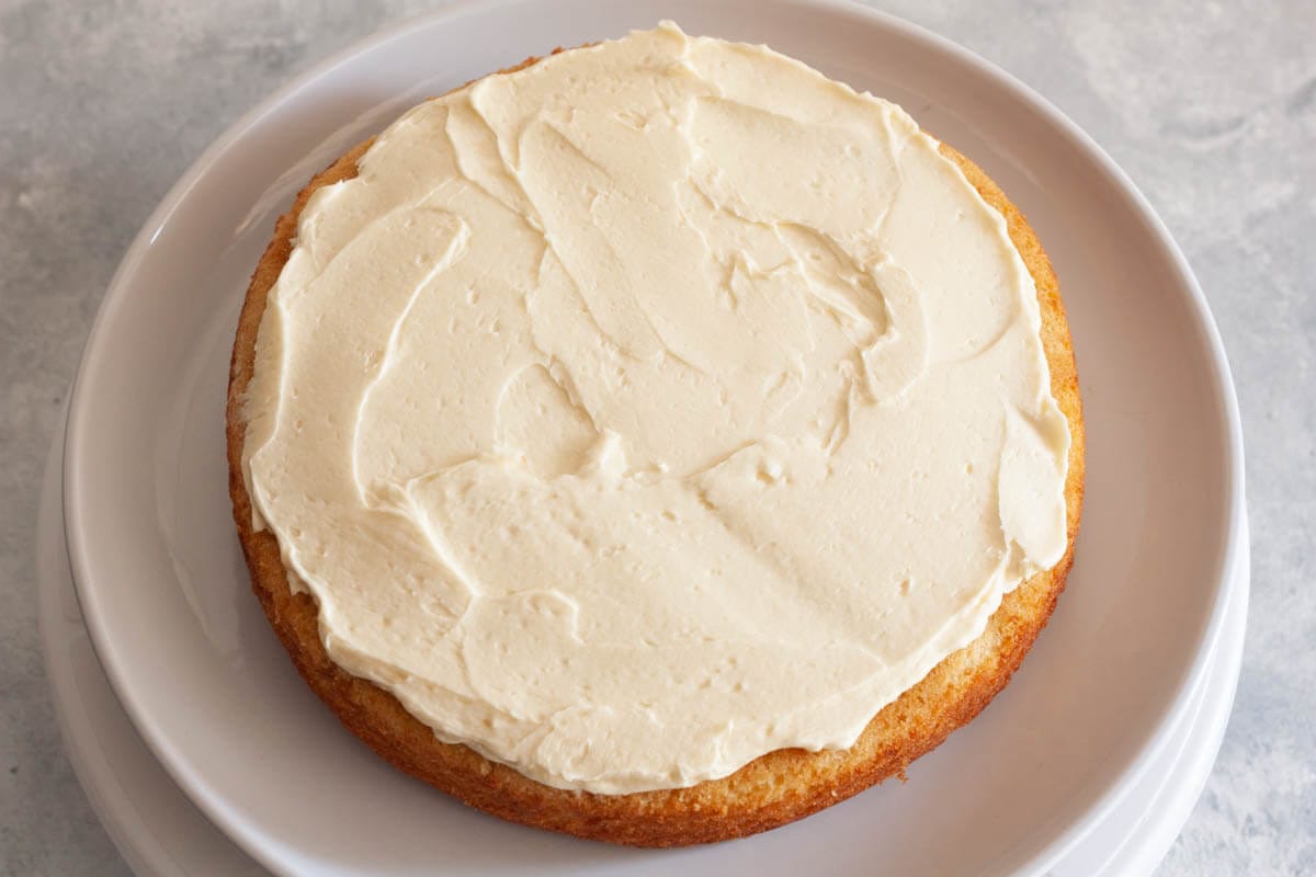 A vanilla cake layer on a white plate topped with vanilla buttercream frosting.