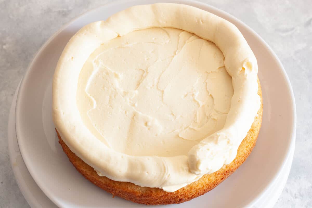 A vanilla cake layer on a white plate topped with vanilla buttercream frosting and a border of frosting around the edge.
