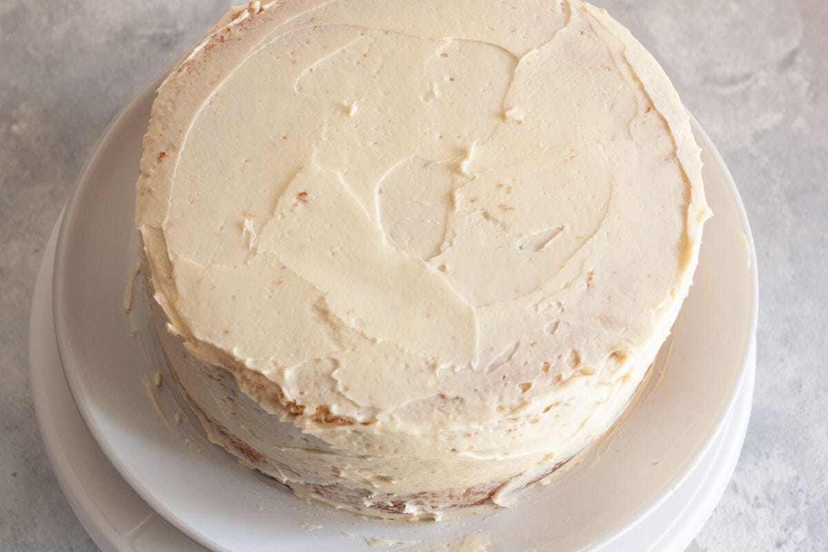 A thin coat of vanilla buttercream frosting all over a two-layer vanilla cake.