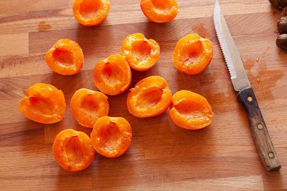 Sliced apricots on a wooden cutting board next to a serrated knife.