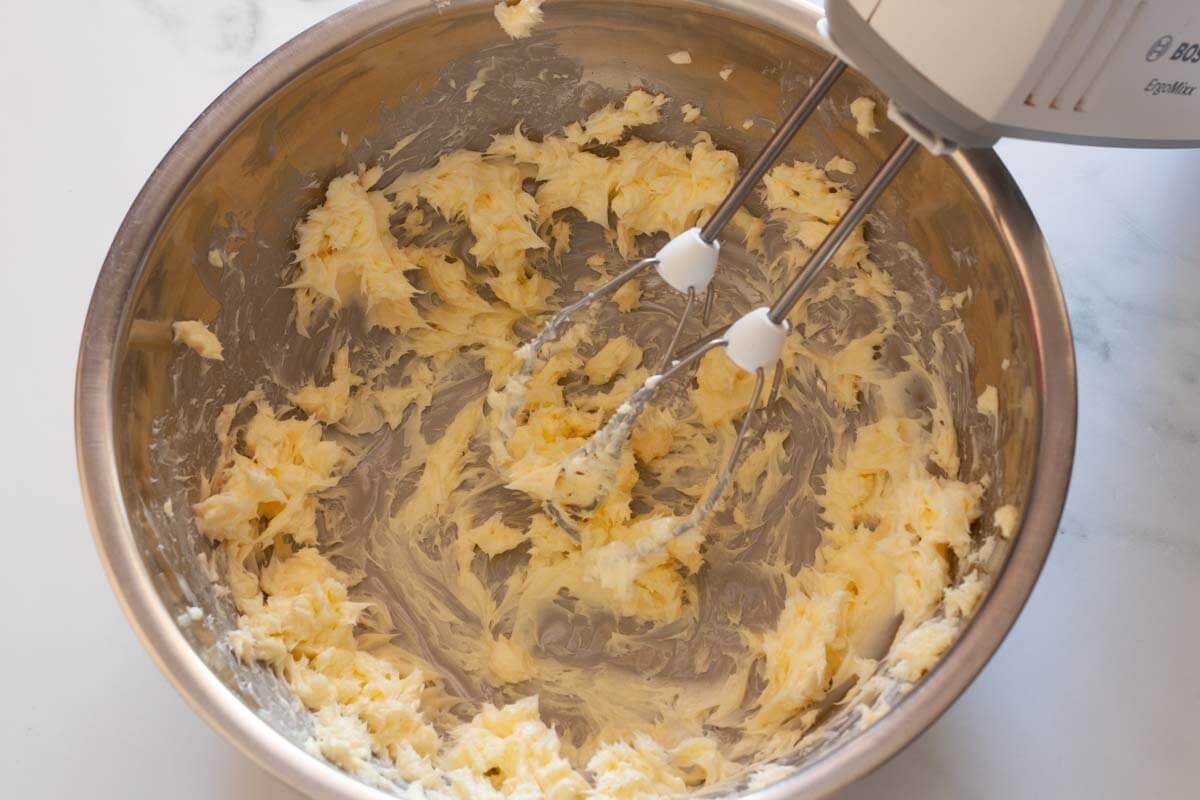 Beating butter with a hand mixer in a metal mixing bowl.