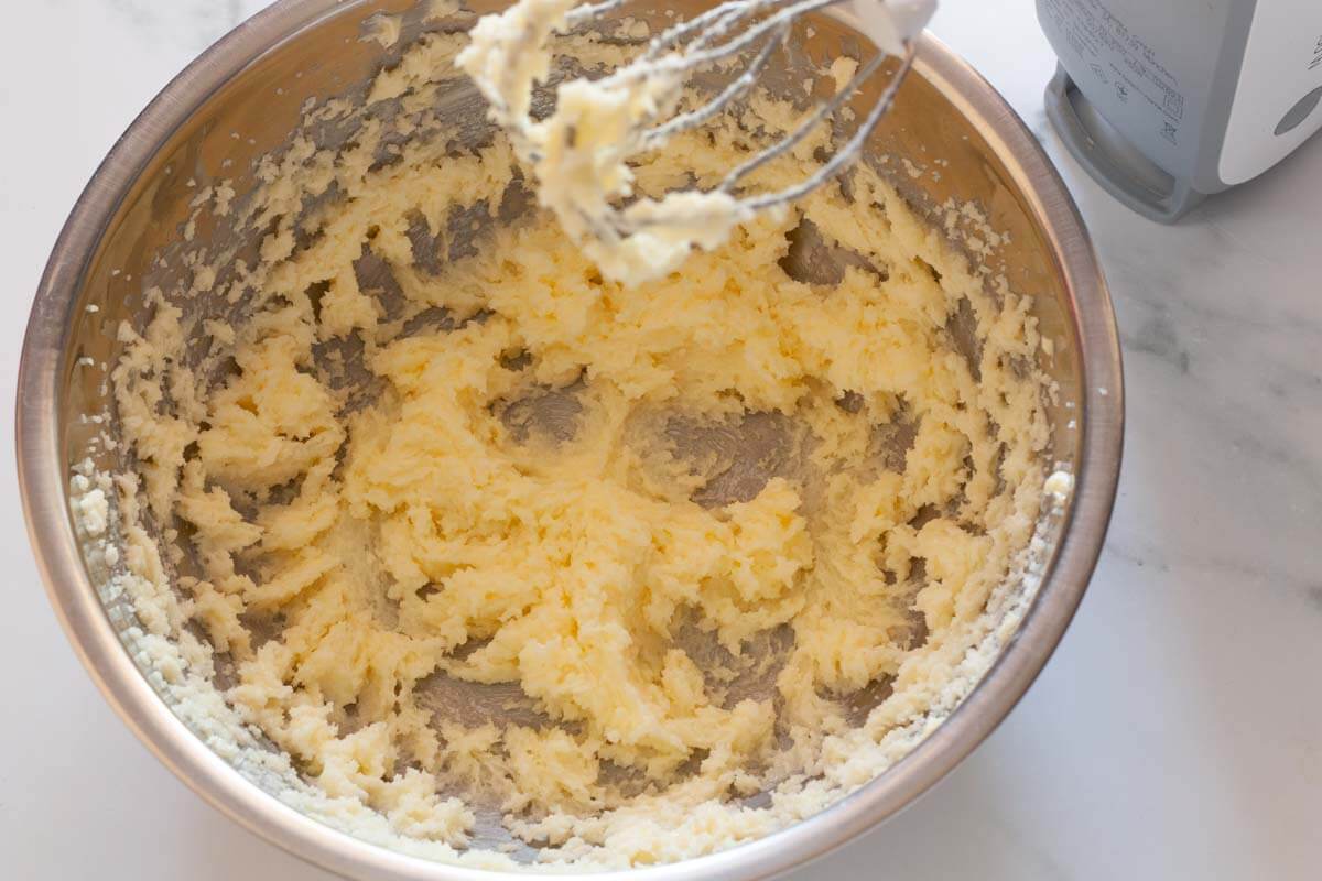 Beating butter and sugar together with a hand mixer in a metal mixing bowl.