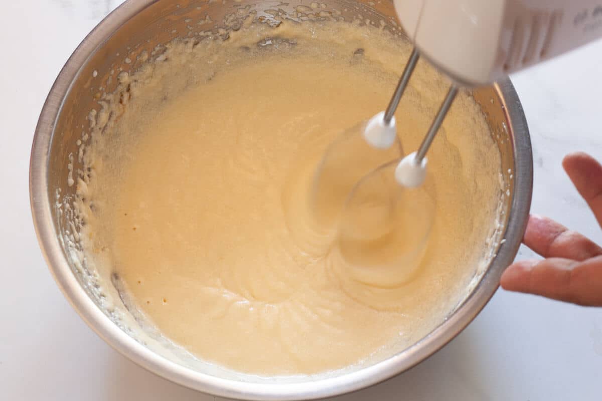 Beating eggs, yogurt and vanilla extract, butter and sugar with a hand mixer in a metal mixing bowl.