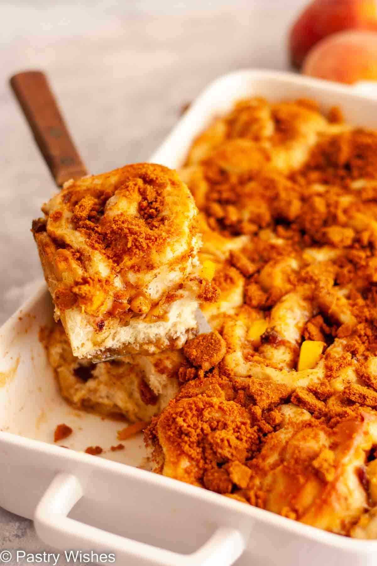 A peach cinnamon roll on a cake server over a pan of peach cinnamon rolls.