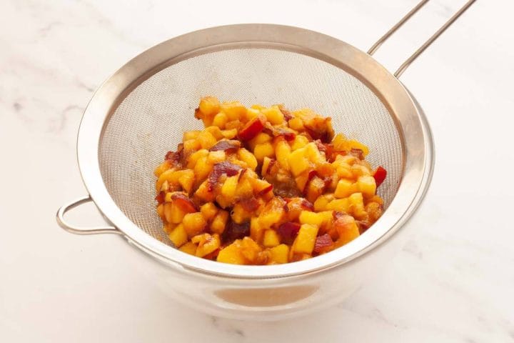 Chopped fresh peaches in a sieve over a glass bowl.