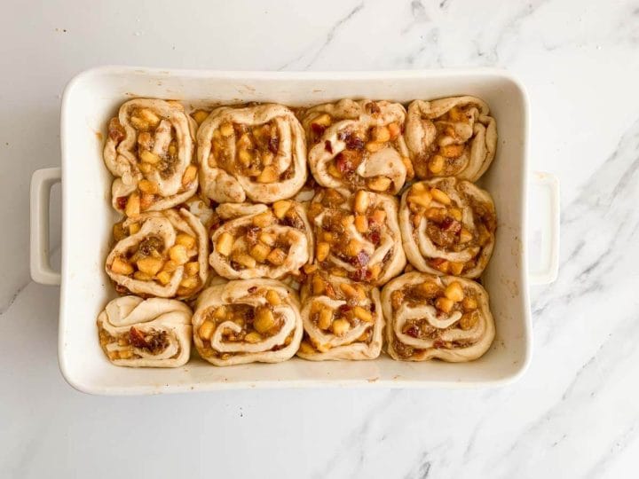 Twelve peach cinnamon rolls in a white baking dish.